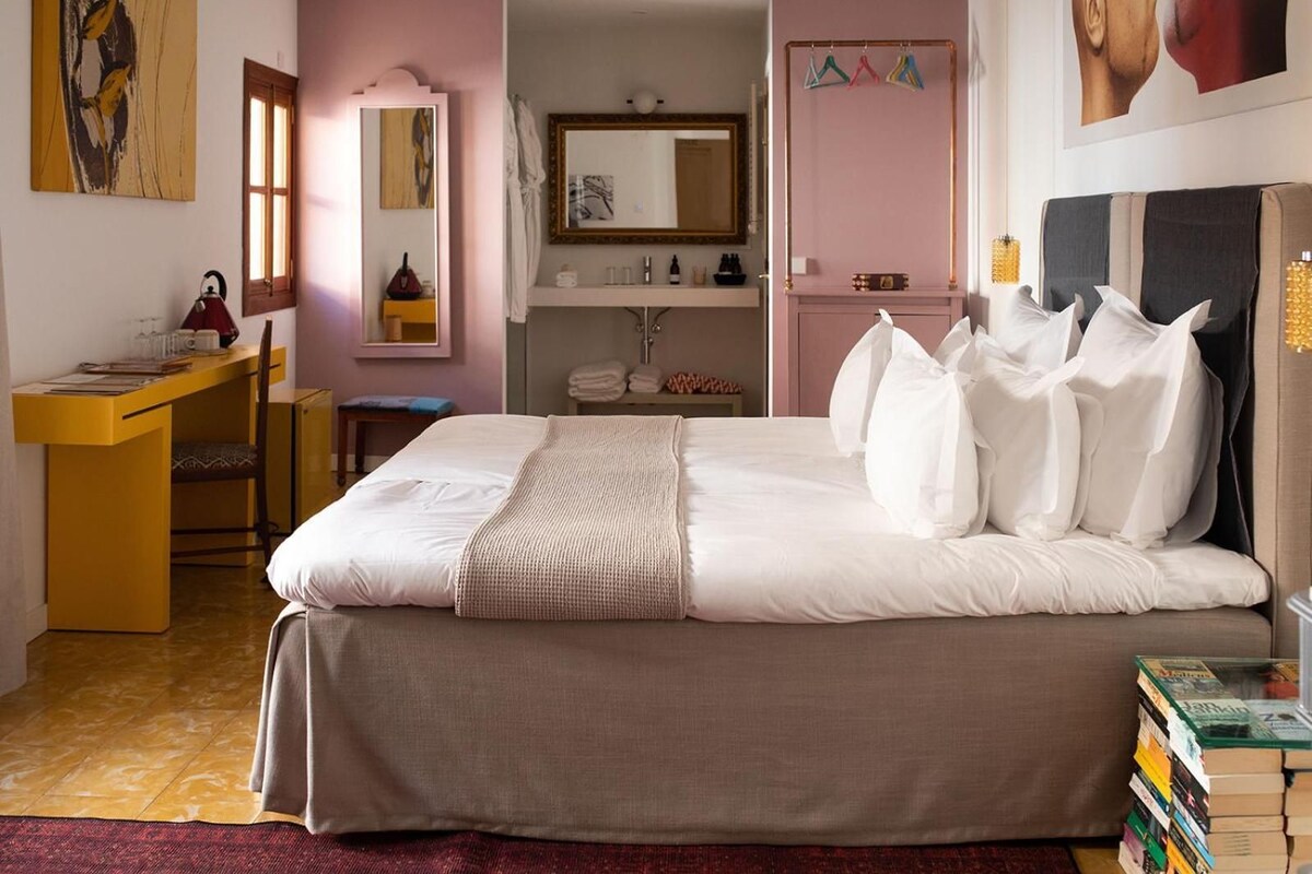 A bedroom with a bed, bedside table, desk, chair, and a mirror.