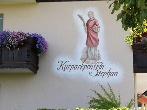 Kurparkpension Stephan features a traditional facade with a striking mural and a charming flower basket.