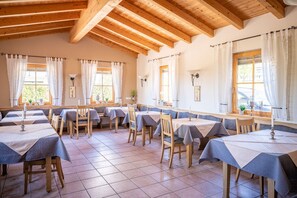 A dining area with multiple tables and chairs, wooden beams on the ceiling, and large windows with curtains. - Appartement Nr. 13, 35 qm Obergeschoss, Wohn- und Schlafraum kombiniert (Bad Endorf)