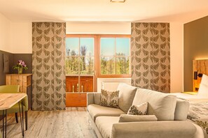 Relax in a serene room with a forest view, featuring a comfortable sofa, desk, and a cozy bed.