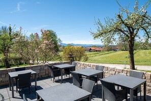Enjoy a serene outdoor space with a stone wall, tables, and chairs overlooking a scenic landscape with views of houses and a hill.