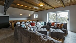 A modern living room with a sectional sofa, a dining area, and a large window providing natural light. - Le Chalets (Falls Creek)