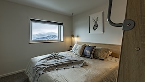 A bedroom with a bed, a window with a mountain view, a headboard, and a wall-mounted light fixture. - Le Chalets (Falls Creek)