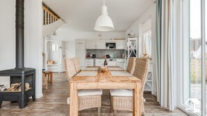 A spacious kitchen with white cabinets, a dining area with a wooden table and wicker chairs, and a large window offering a view of the outdoors.