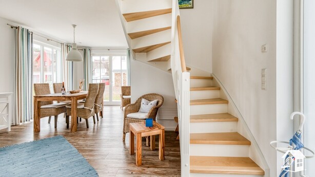 A spacious living area with a wooden staircase, wicker furniture, and a dining table.