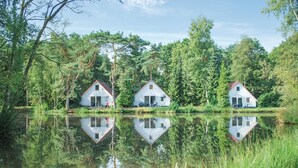 Three white houses with red roofs, each with a small porch and a single window, situated by a calm lake surrounded by dense greenery. - 3 bedroom nice home in Vledder (Vledder)