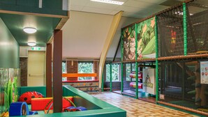 A children's play area with colorful play structures and a large window with a view of trees. - 3 bedroom nice home in Vledder (Vledder)