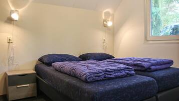 A bedroom with two beds, a nightstand, and wall-mounted lights.