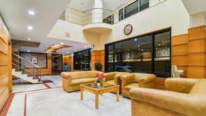 A lobby with a staircase, leather sofas, a glass coffee table, and a clock on the wall. - Grand Plaza (Coimbatore)