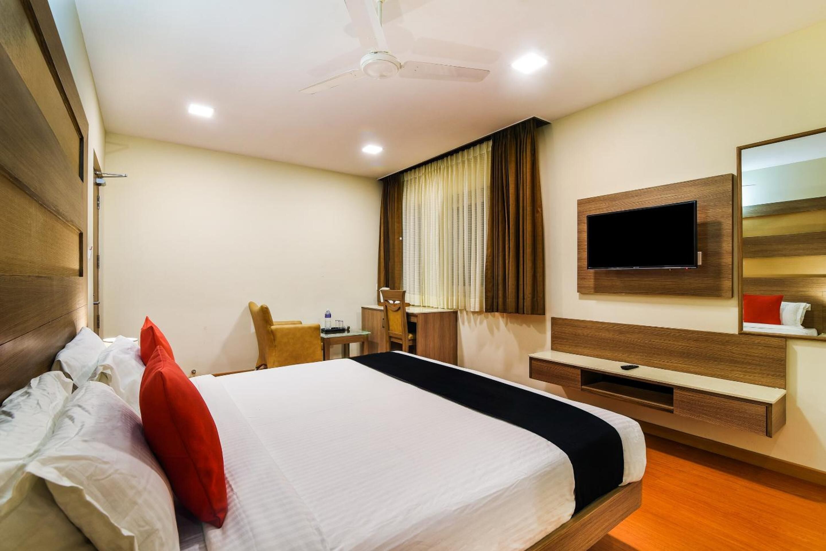 A hotel room with a bed, a desk, a chair, a television, and a ceiling fan.