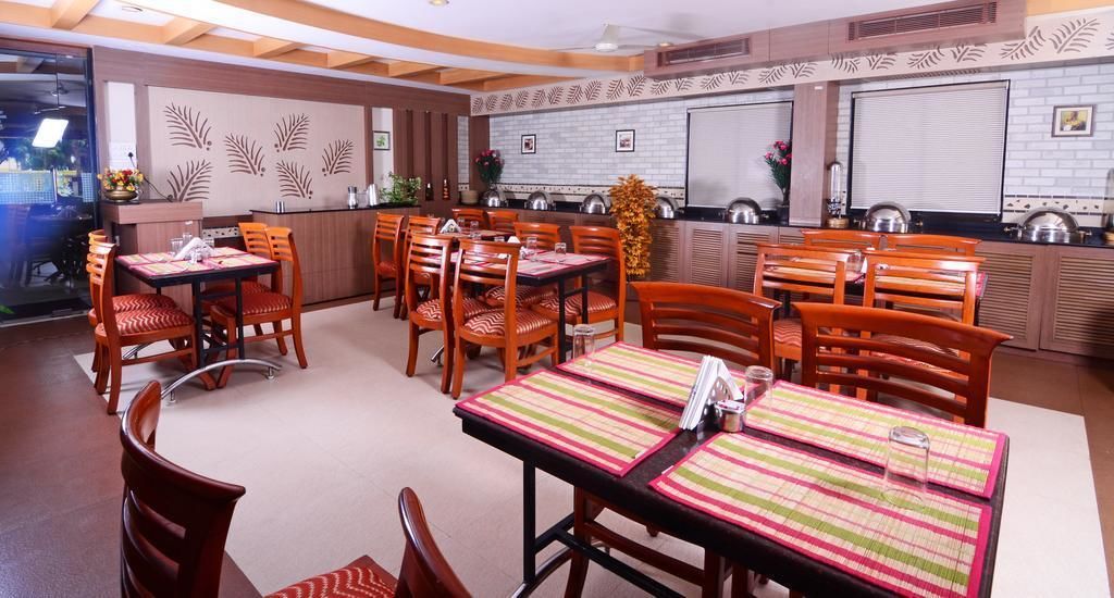 A dining area with multiple tables and chairs, a kitchen in the background, and decorative wall patterns.