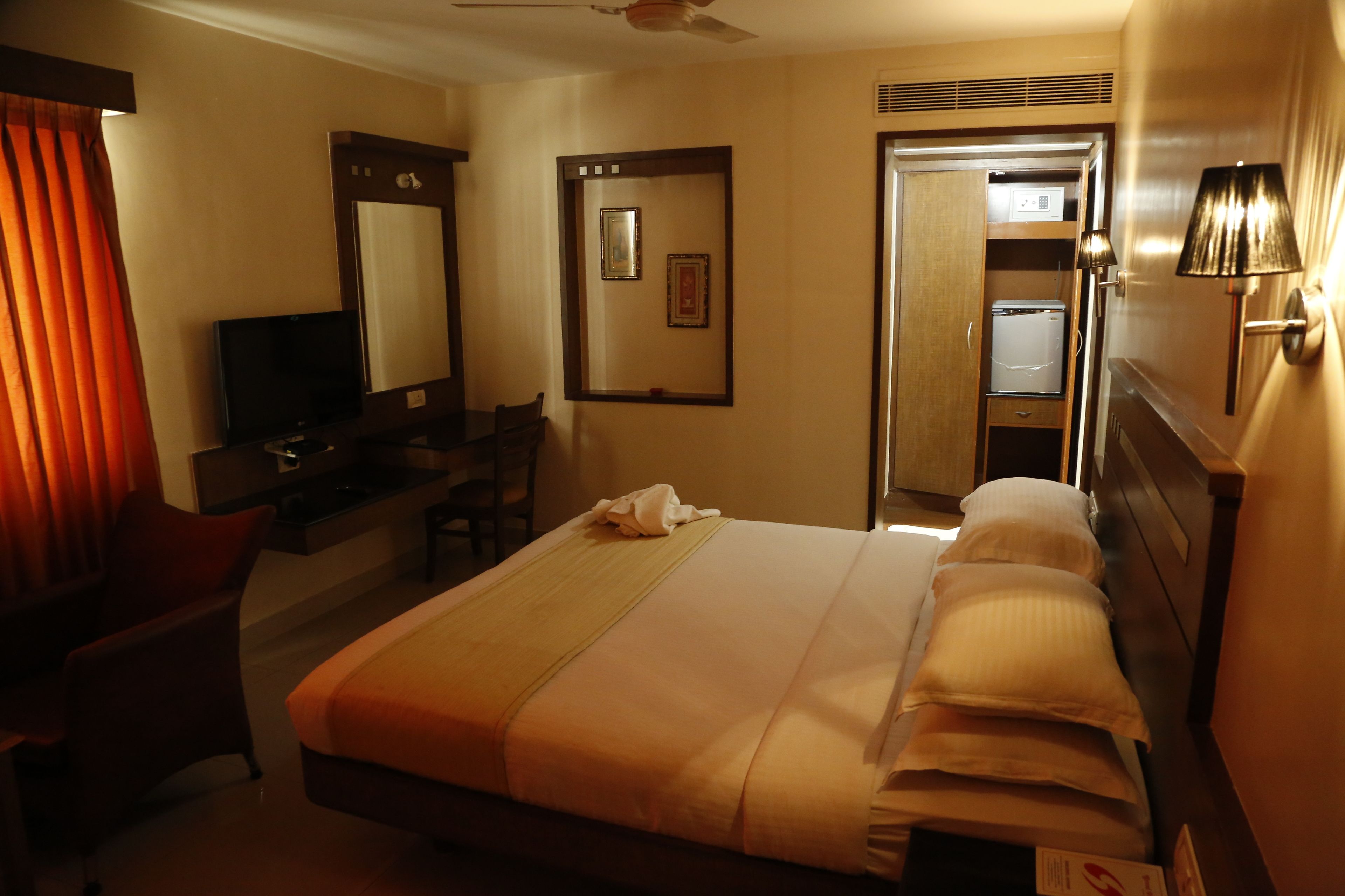 Habitación de hotel con cama, escritorio con televisor, silla, espejo y puerta que da a un baño.
