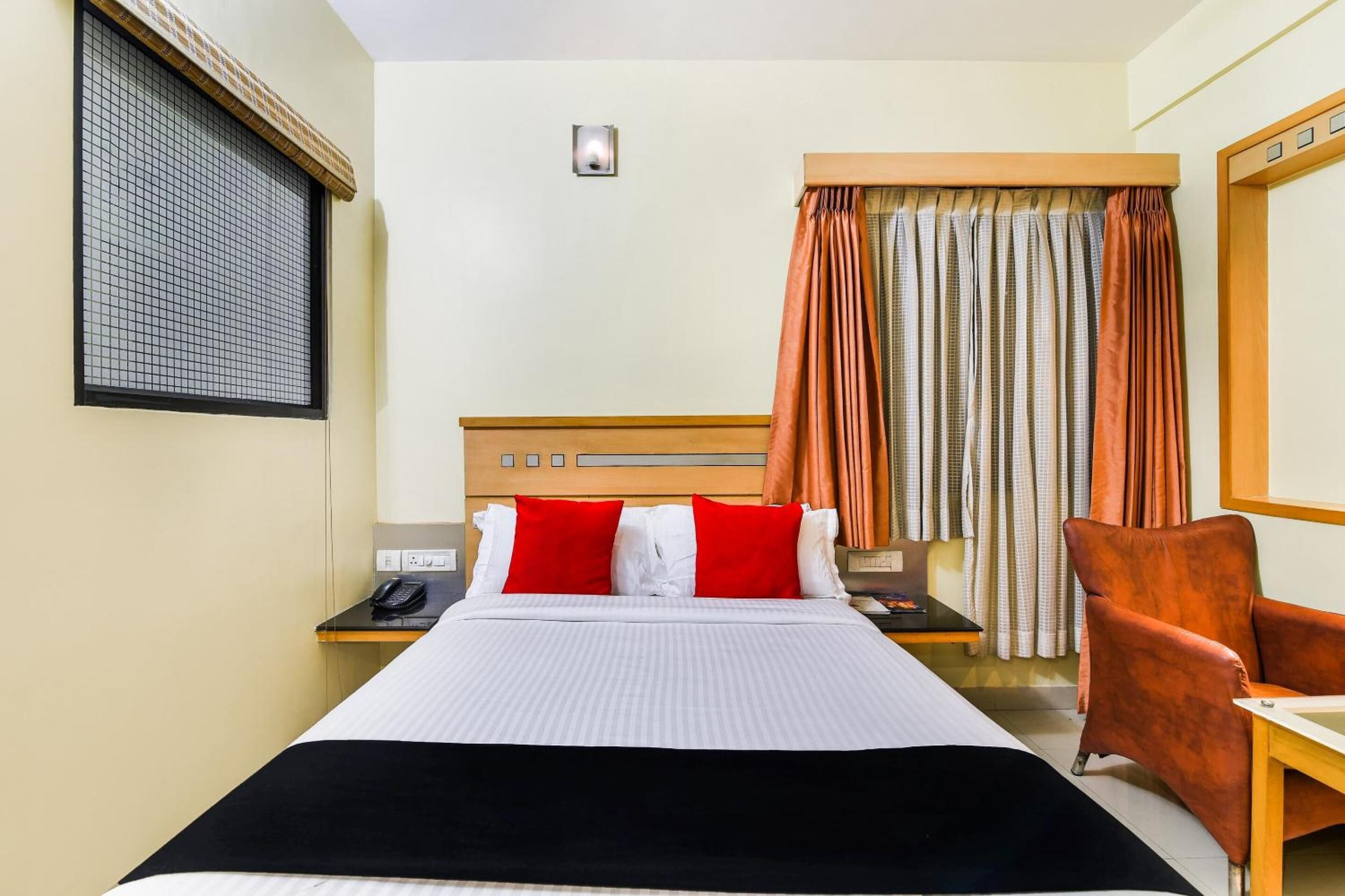 Une chambre d’hôtel avec un lit, un bureau, une chaise, un téléphone et une fenêtre avec des rideaux.
