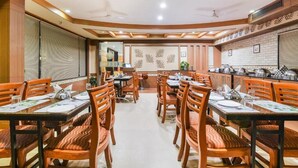 A restaurant with wooden tables and chairs, a kitchen area, and a decorative wall with leaf patterns. - Grand Plaza (Coimbatore)