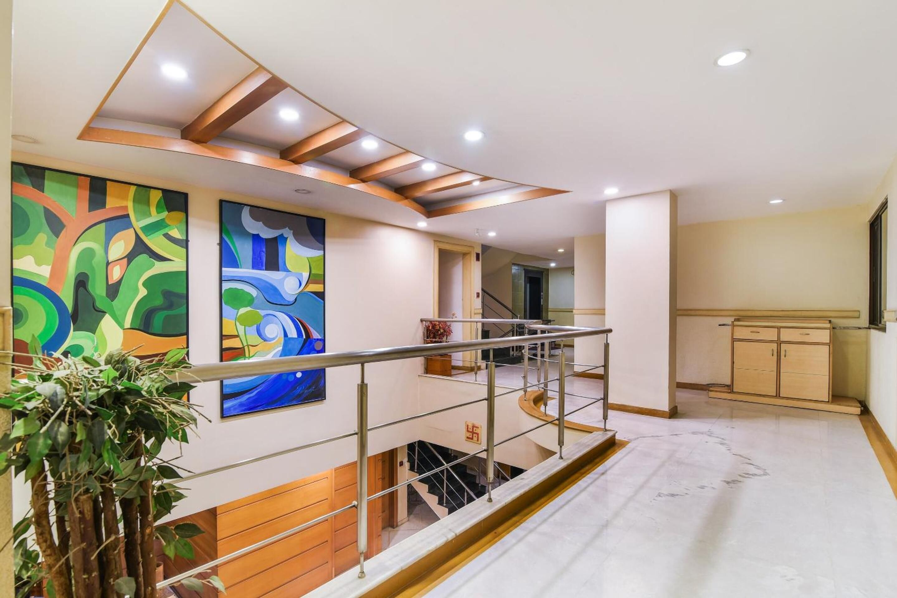 Um interior moderno com uma escada, um corrimão de madeira e duas pinturas abstratas na parede.
