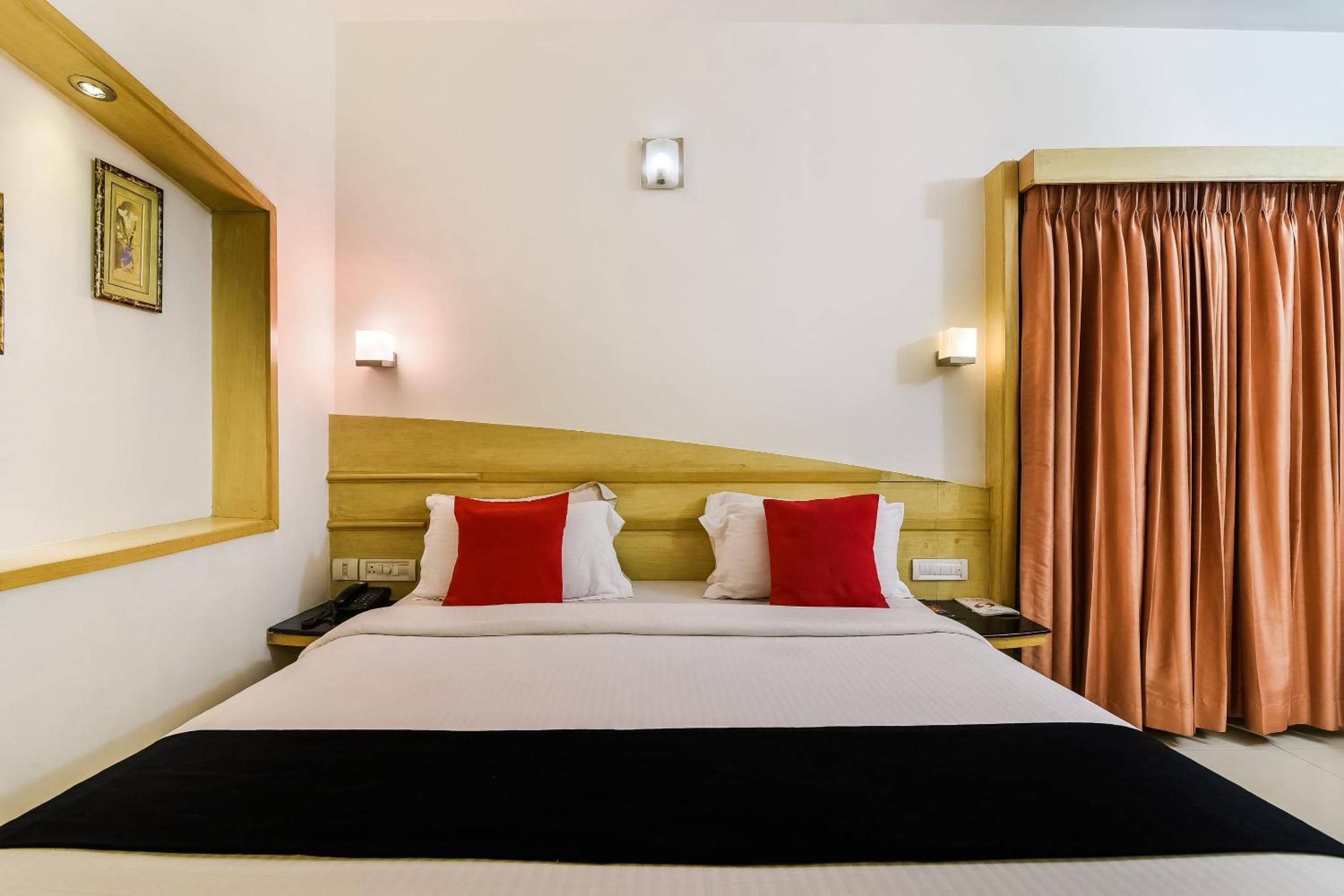 Habitación de hotel con una cama grande, dos mesitas de noche, un cabecero de madera y vista a una cortina.