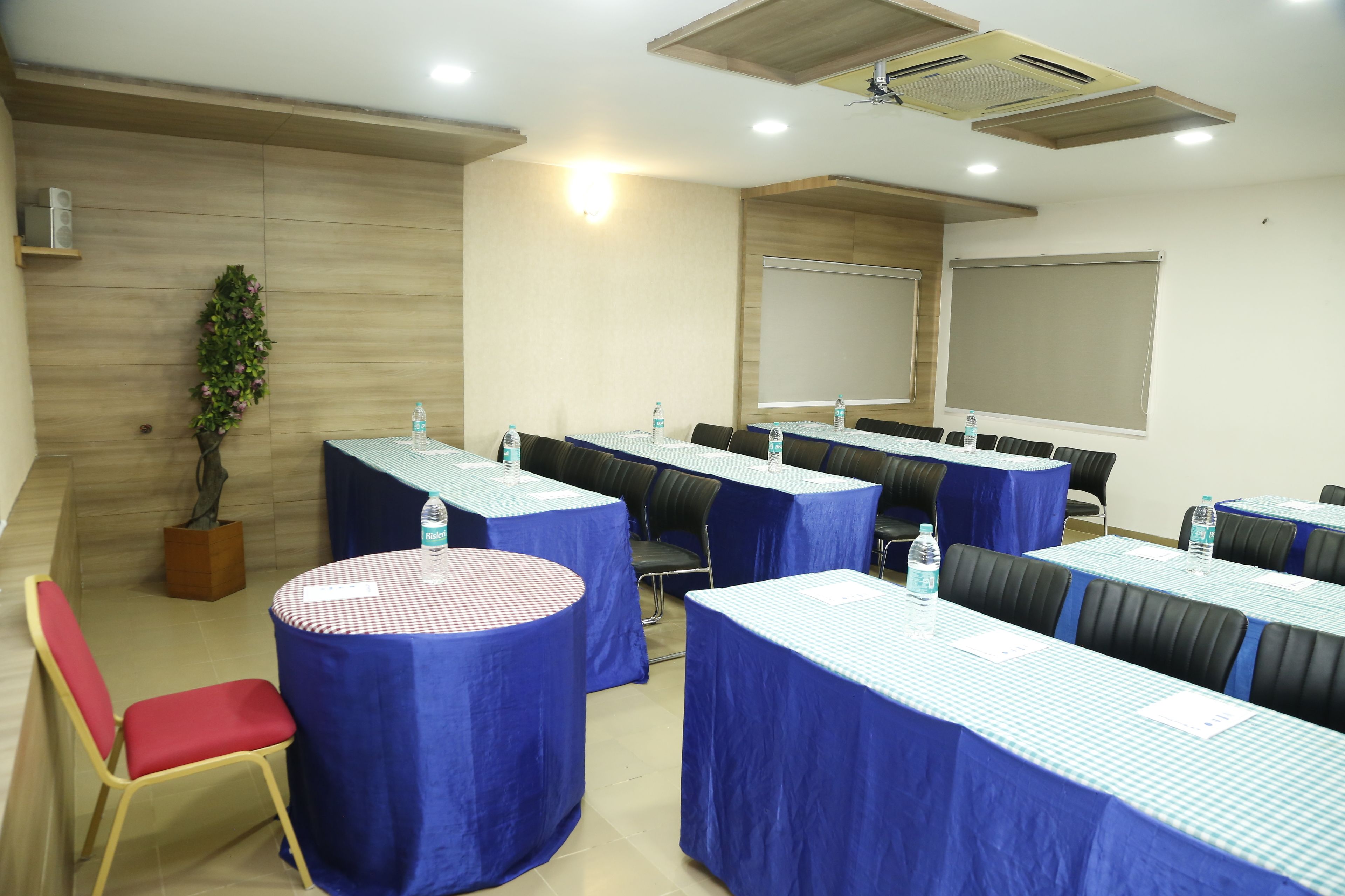 A conference room with round and rectangular tables covered with blue tablecloths, equipped with water bottles, and surrounded by chairs.