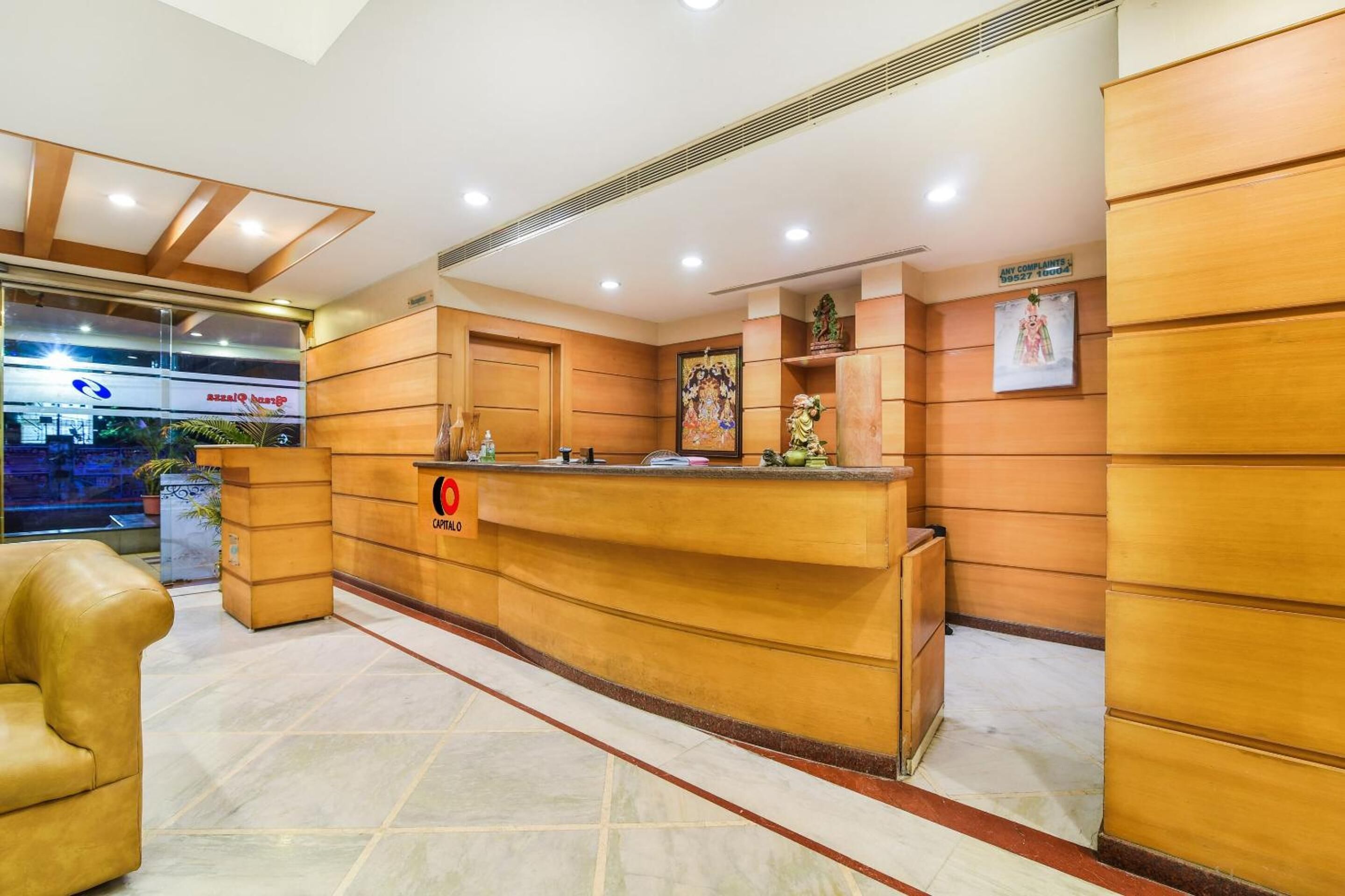 A hotel reception area with a wooden reception desk, a sign for complaints, and a view of the outside.