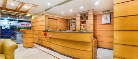 A hotel reception area with a wooden reception desk, a sign for complaints, and a view of the outside.