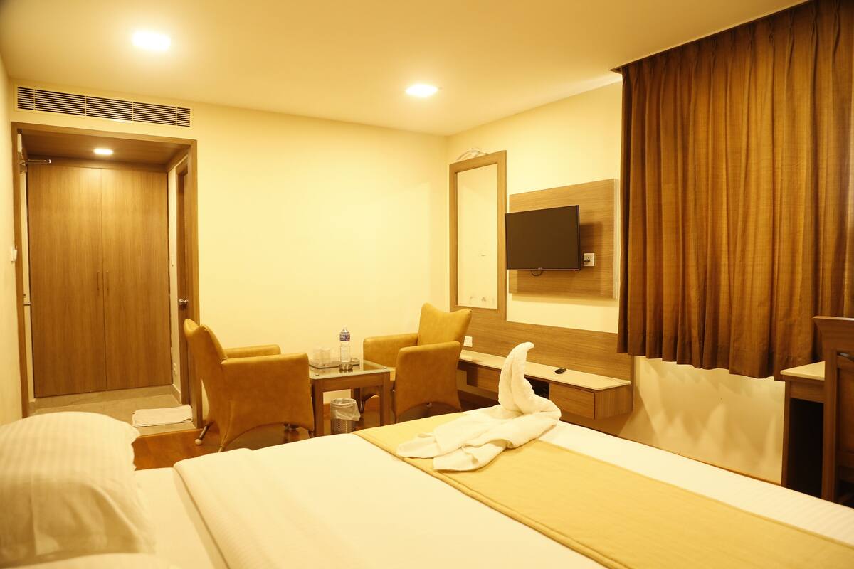 A hotel room with a bed, two chairs, a desk, a television, and a mirror.