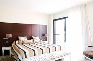 A modern hotel room with a large bed, bedside tables, a bench, and a view of the outdoors. - Mar d'Espills (Amposta)