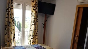 A bedroom with a bed, curtains, a television, and an air conditioning unit. - Hotel Mas Subirats (Mora la Nova)
