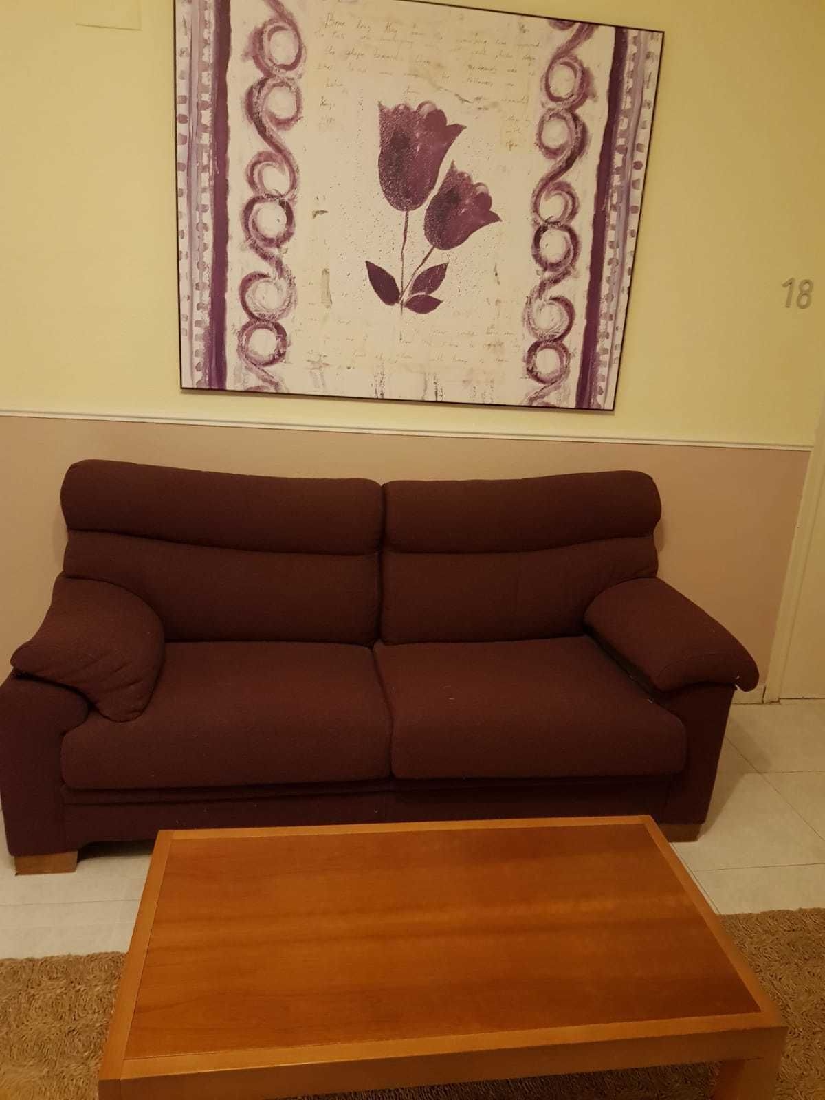 A brown sofa and a wooden coffee table in a room with a wall-mounted artwork featuring a flower and the number 18.