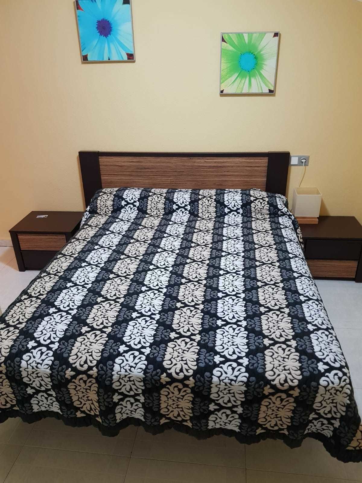 A bed with a black and white patterned bedspread, two bedside tables, and two wall-mounted lamps.