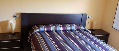 A hotel room with a bed, two bedside tables, a wall-mounted artwork, and a nightstand with a lamp.