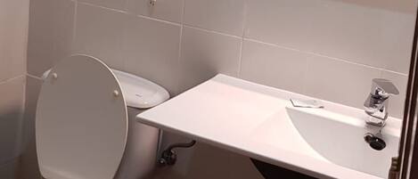 A bathroom with a toilet, a sink, and a hairdryer mounted on the wall.