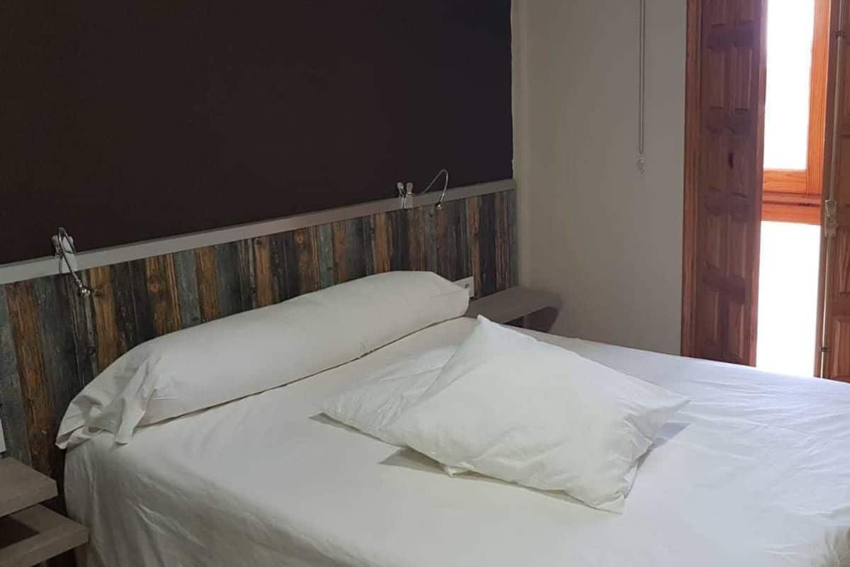 Una cama con ropa de cama blanca en una habitación con puerta de madera y ventana.