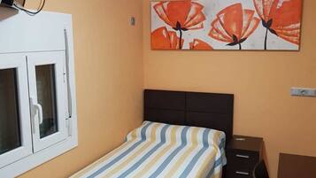Een slaapkamer met een bed, een bureau, een stoel, een raam met jaloezieën en een schilderij aan de muur.
