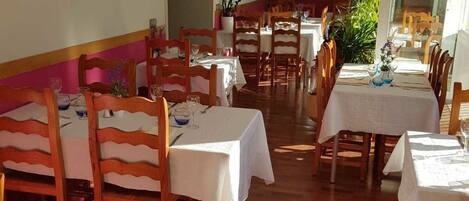 Un área de comedor con sillas y mesas de madera, un cuadro en la pared y una planta en maceta.