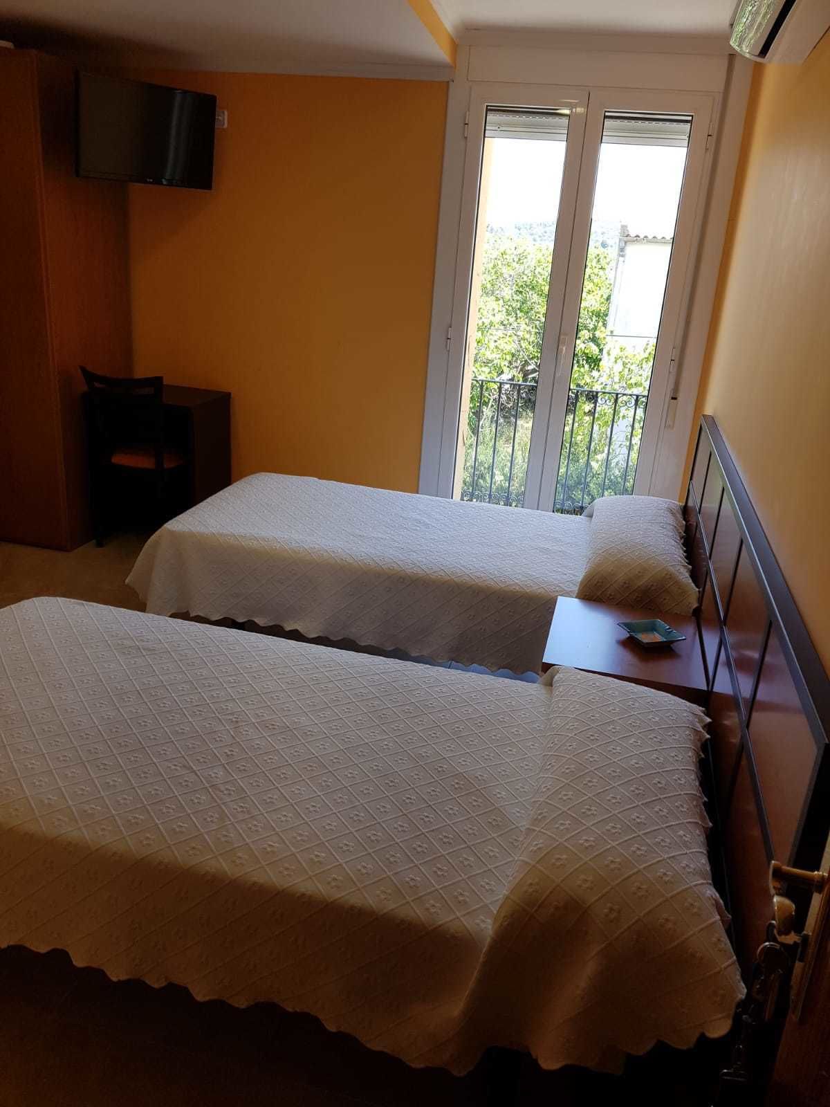 Una habitación con dos camas, un televisor montado en la pared y un balcón con vistas.