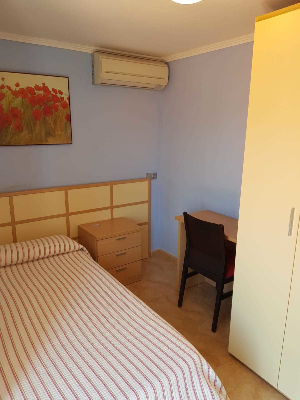 Um quarto com cama, escrivaninha e guarda-roupa.