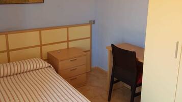 Um quarto com cama, escrivaninha e guarda-roupa.