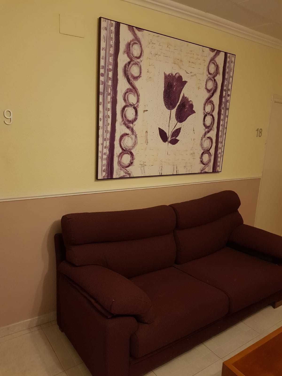Una sala de estar con un sofá marrón y una obra de arte enmarcada en la pared.