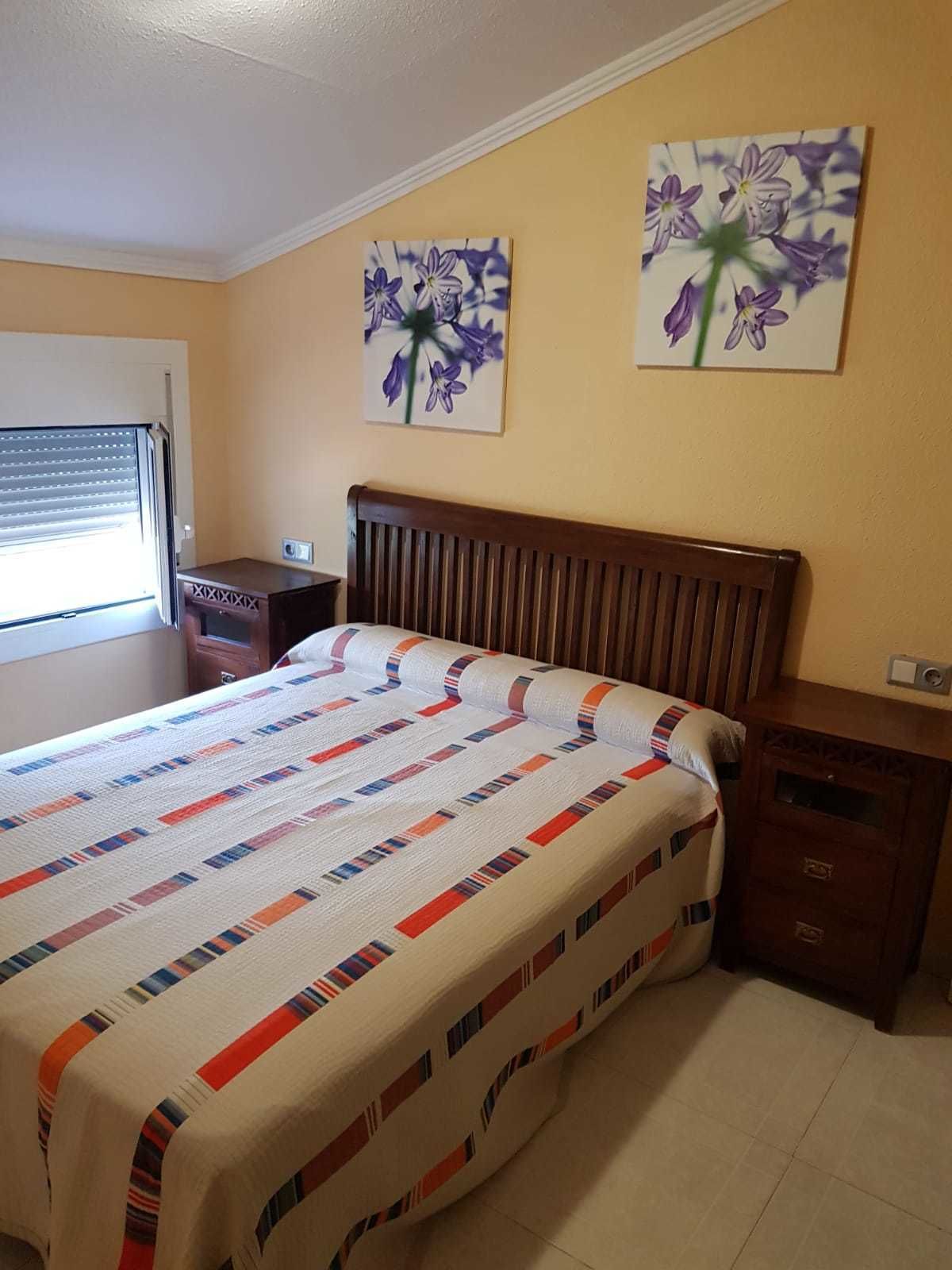 Une chambre à coucher comprenant un lit, une table de chevet, une commode et deux tableaux représentant des fleurs, accrochés au mur.