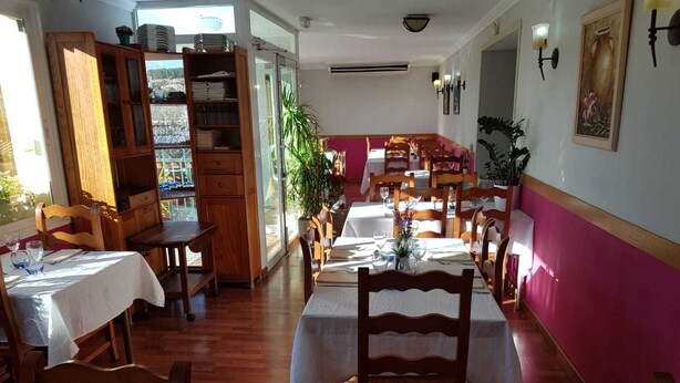 A dining area with wooden tables and chairs, a kitchen area with cabinets, and a view of the outside through a glass door. - Hotel Mas Subirats (Mora la Nova)