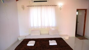 Un dormitorio con una cama grande, paredes blancas, una ventana con cortinas traslúcidas y un espejo en la pared.