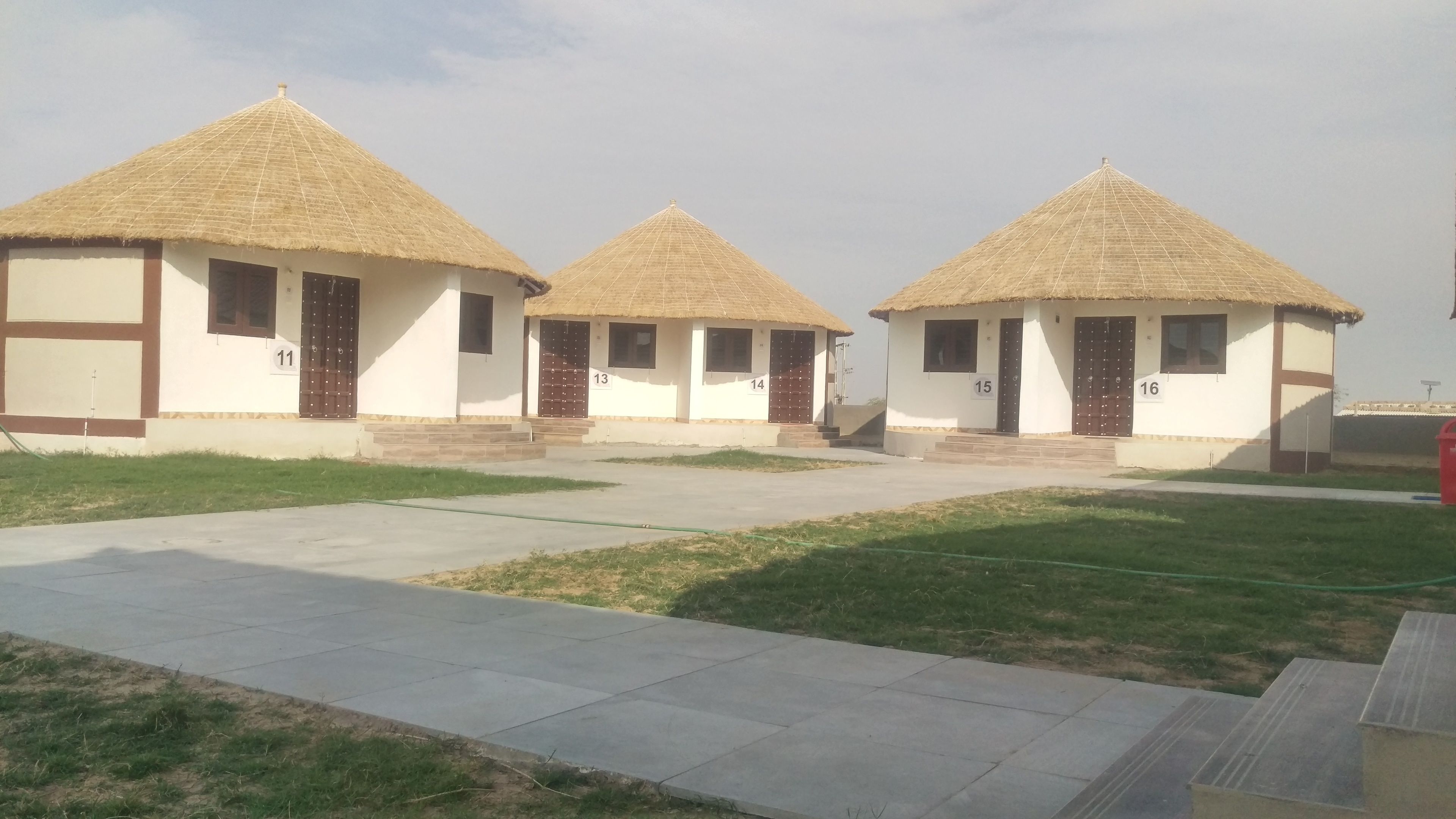 Une rangée de maisons aux toits de chaume, numérotées de 11 à 16, avec un trottoir dallé devant.