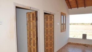 Un pasillo con dos puertas de madera, una ventana y vista a una zona arenosa afuera.
