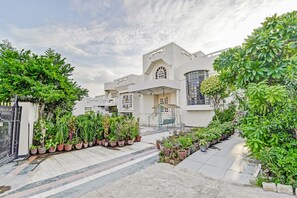 A modern building with a central entrance, surrounded by potted plants and a paved walkway. - Abode Homestay (Jaipur)