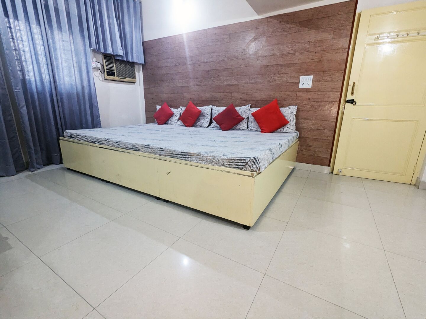 A bedroom with a bed, a wooden headboard, a door, and a window with curtains.