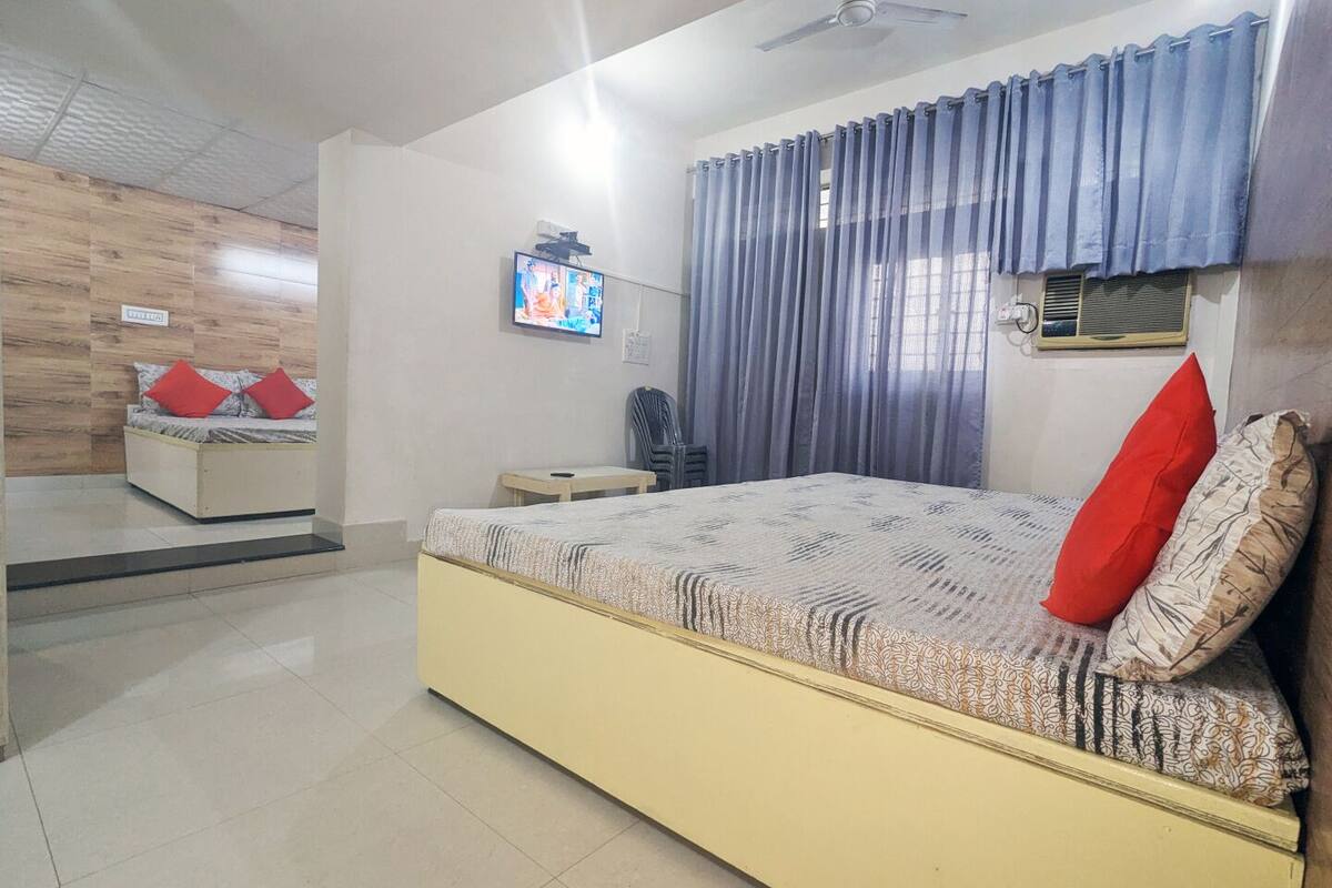 A bedroom with a bed, a TV, a ceiling fan, and a window with curtains.