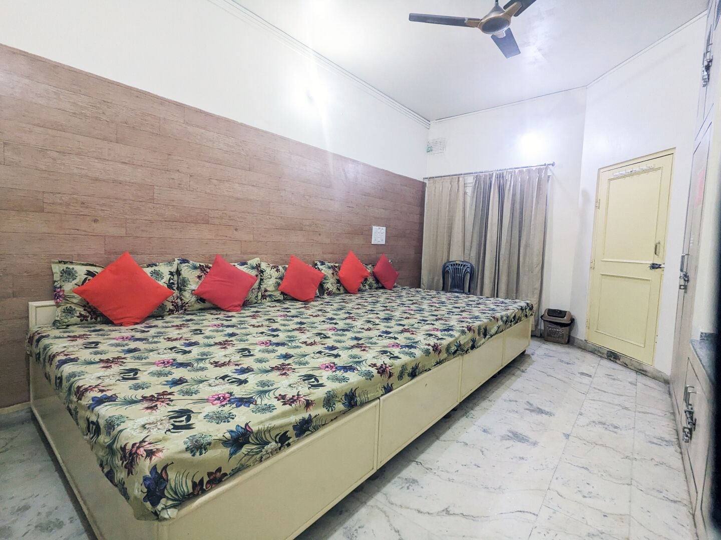 Um quarto com cama, ventilador de teto, porta e janela com cortinas.