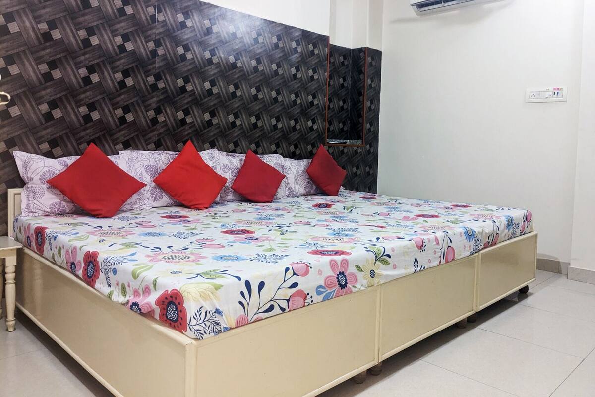 A bed with a floral bedspread, red pillows, and a headboard with a geometric pattern.