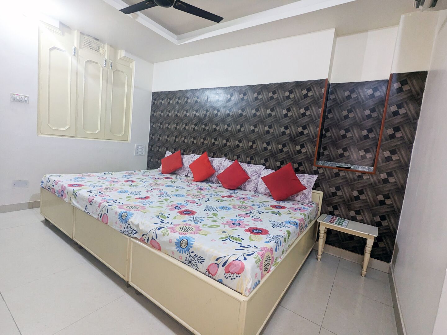 Un dormitorio con cama, una mesita de noche pequeña, ventilador de techo y ventana con cortinas.