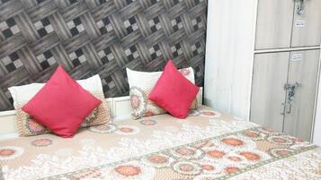 Una cama con colcha estampada y dos almohadas rojas, una pared a cuadros y un armario blanco de dos puertas.