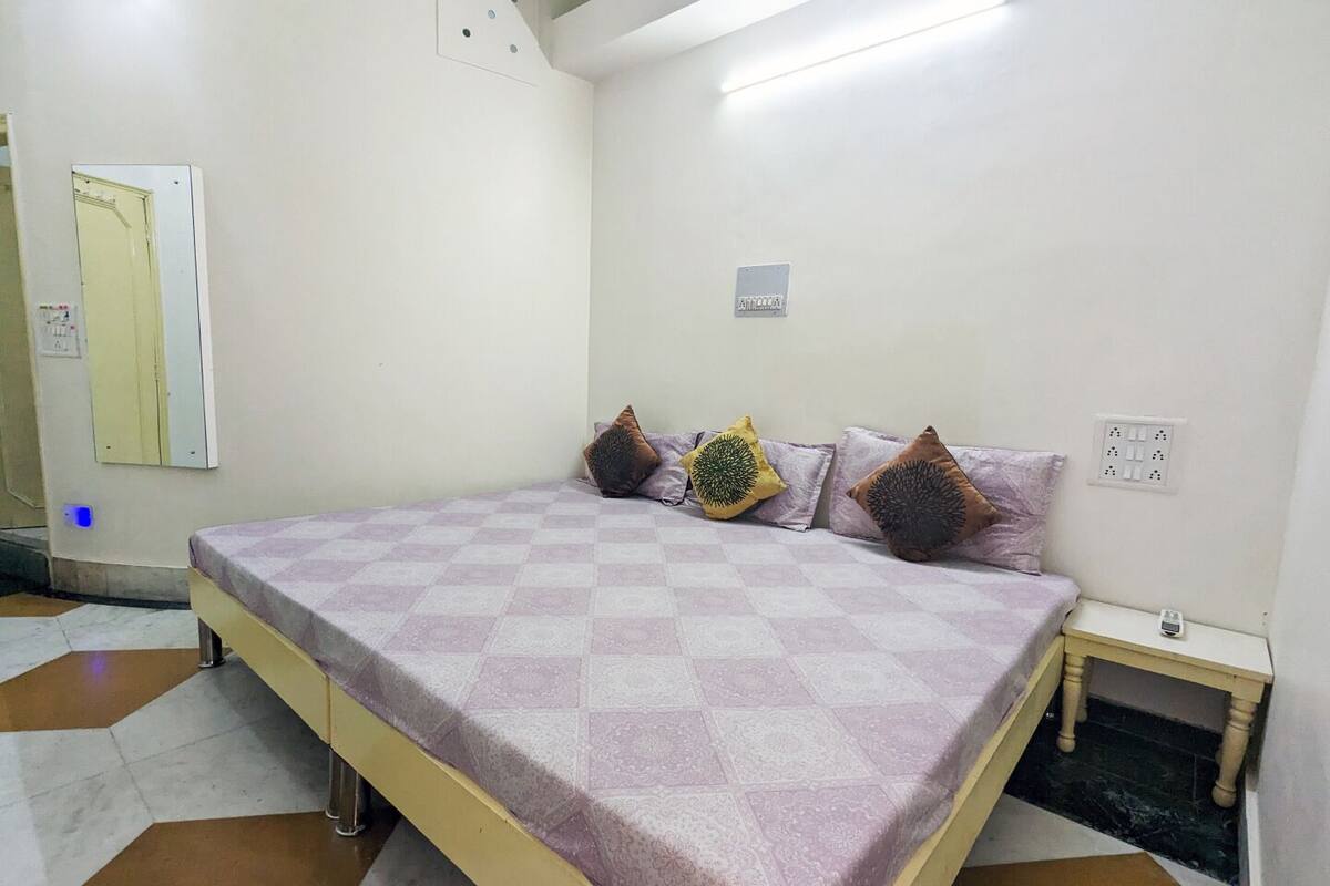 A bedroom with a bed, a nightstand, a mirror, and a wall socket.